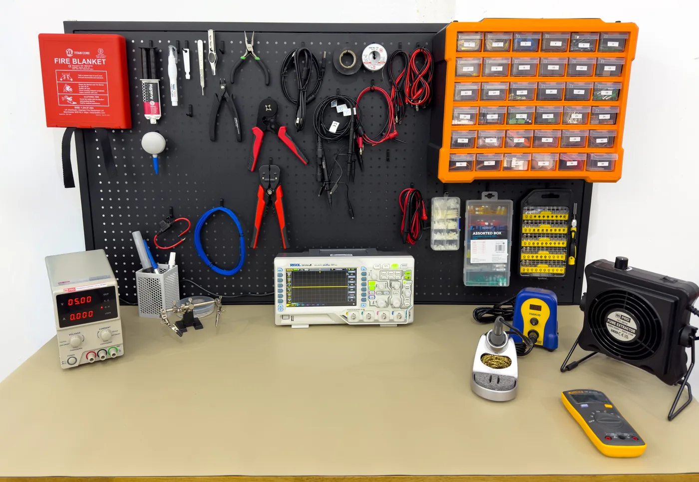 Electronics bench with oscilloscope, soldering tools, power supply, test leads, and component storage